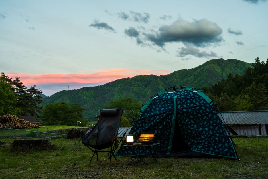 テント、椅子、ランタンが置かれた静かなキャンプ風景。背景には絵のように美しい山の夕日が広がる。